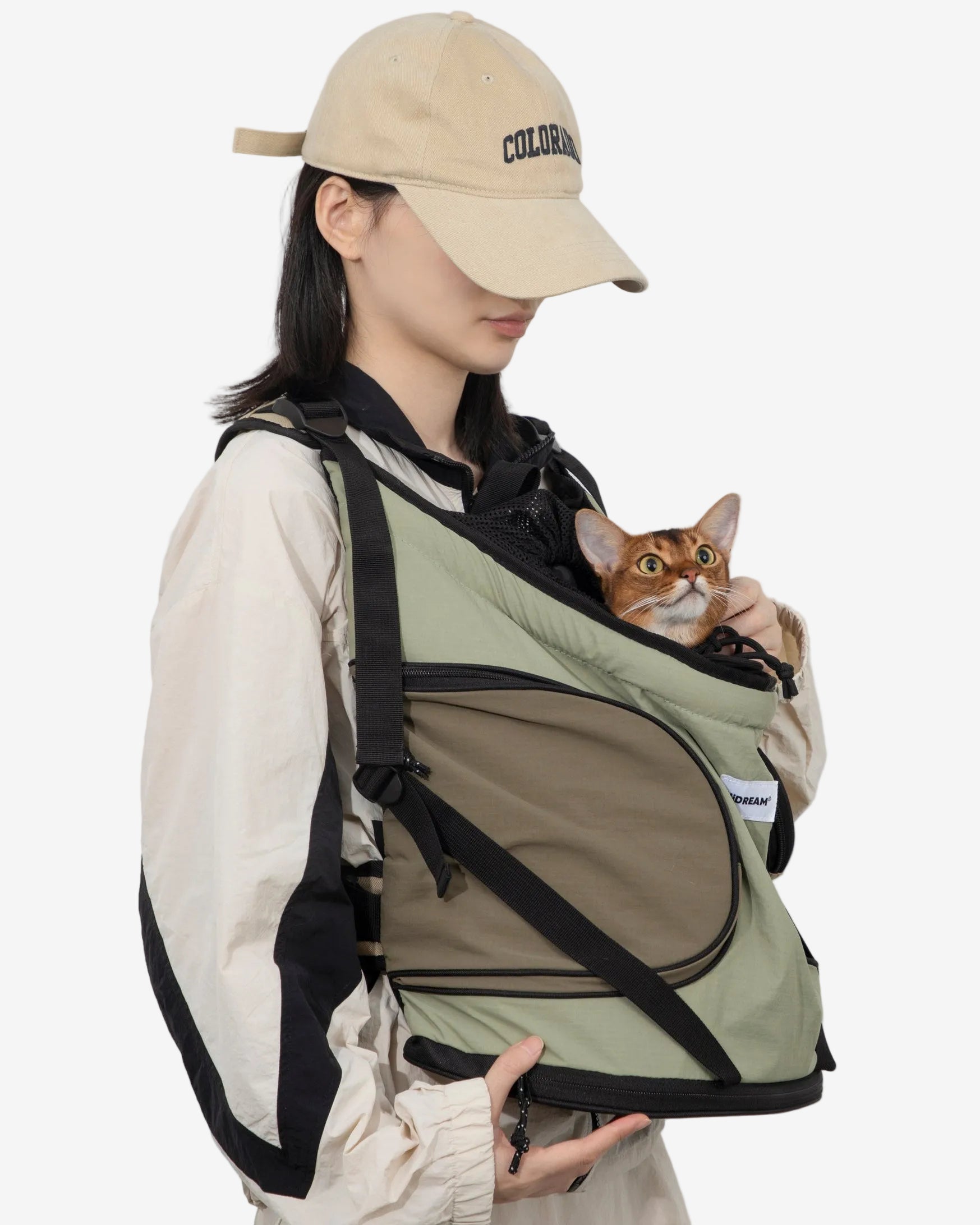 Person wearing a green pet carrier with a cat inside, against a plain background