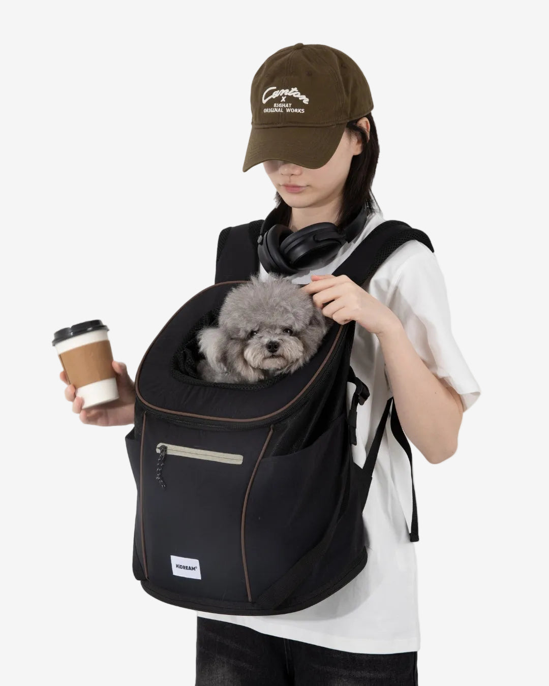 Person carrying a small dog in a black backpack while holding a coffee cup on a white background