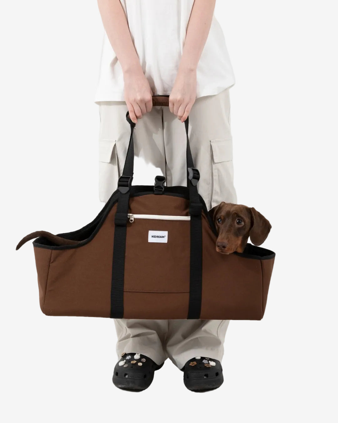 Person holding a brown pet carrier with a dog peeking out, on a white background